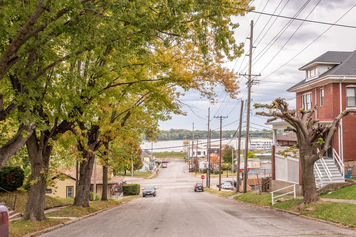 A tree-lined street stretches toward a picturesque view of the river, with classic residential architecture framing the scene. The vantage point hints at a community rich with history and provides a sense of place and connection to the Mississippi.